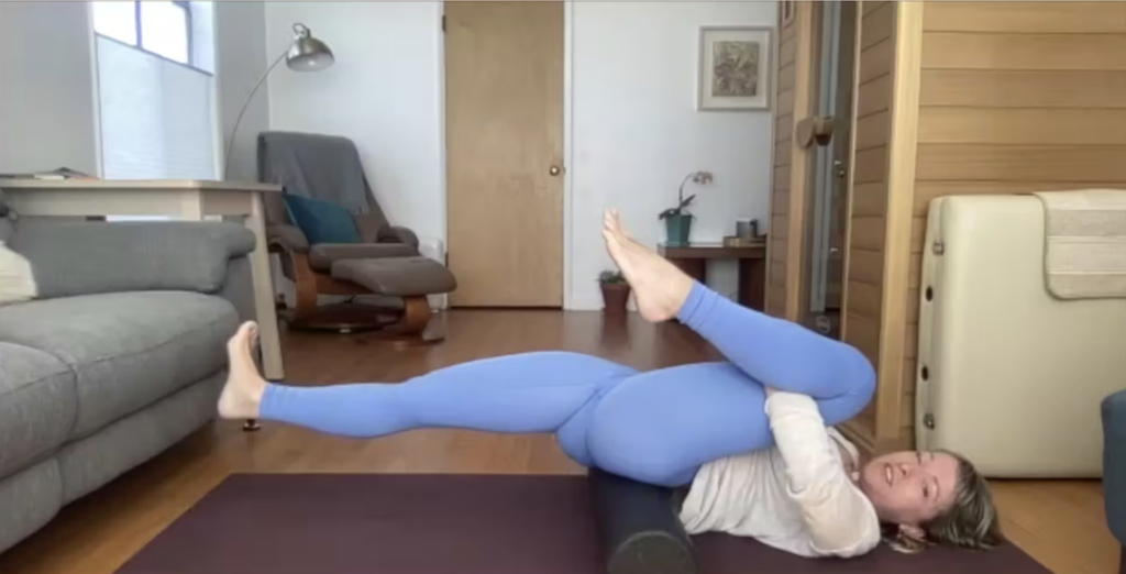 Woman doing Pilates exercises on the Pilates mat with a foam roller under her low back.