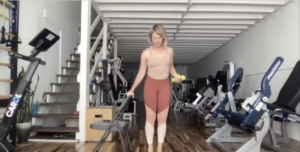 Woman doing standing Pilates exercises holding weights. There is a chair next to her that she is holding.