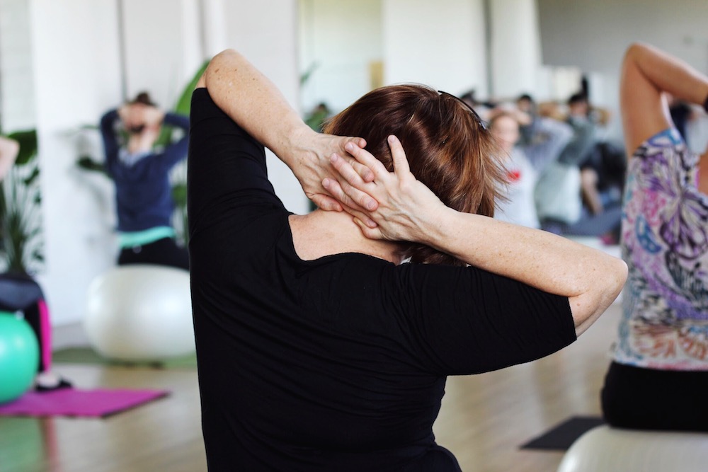 Close up of woman doing Pilates for pain reduction in a class seated on a Pilates ball.