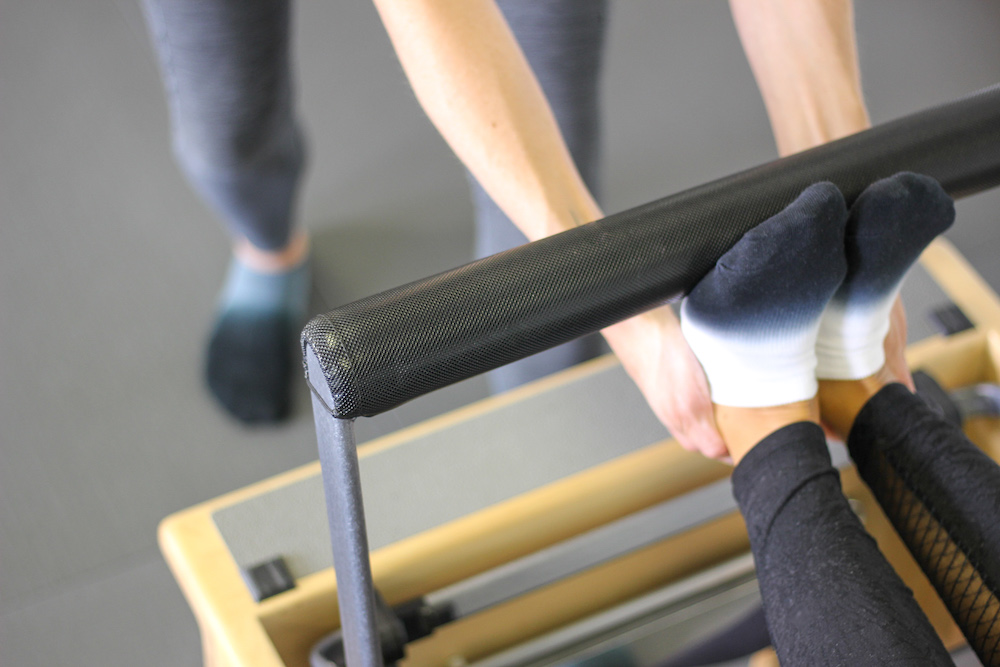 Woman helping another woman with Pilates stretches on the Pilates reformer.