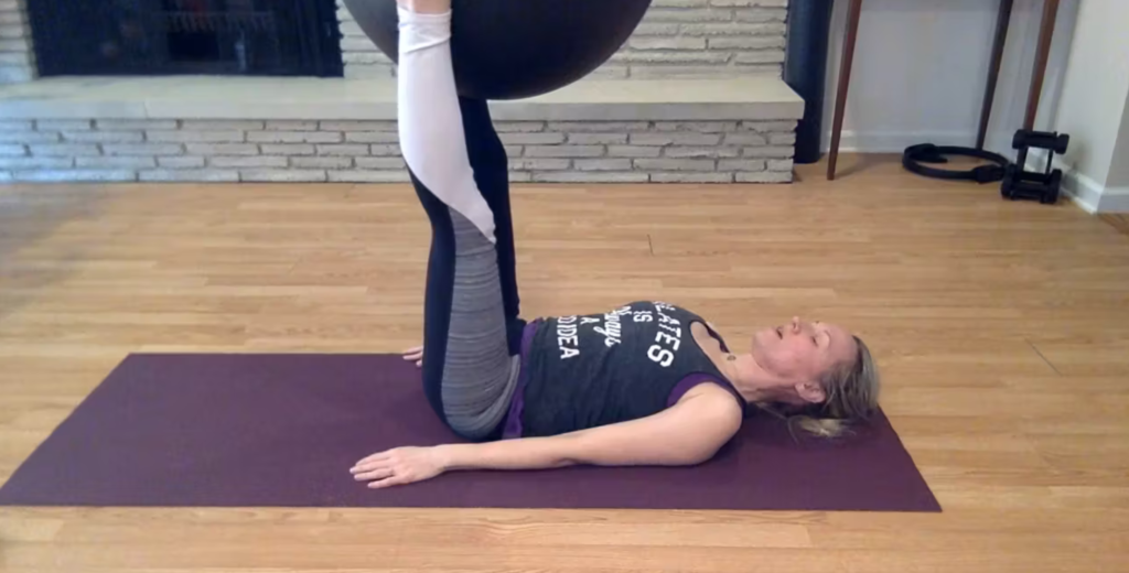 Woman doing Pilates exercises on a yoga mat with a Pilates ball.