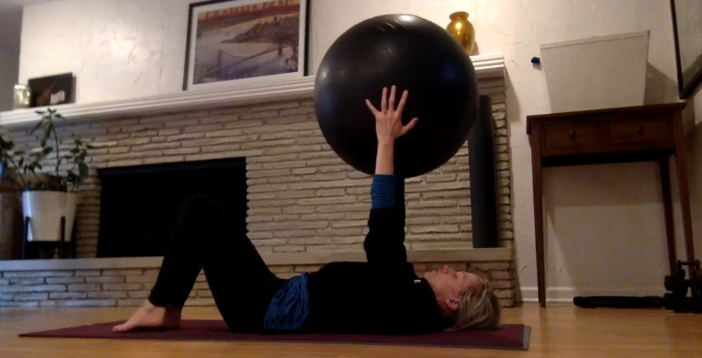 Woman doing Pilates exercises on a yoga mat with a Pilates ball.