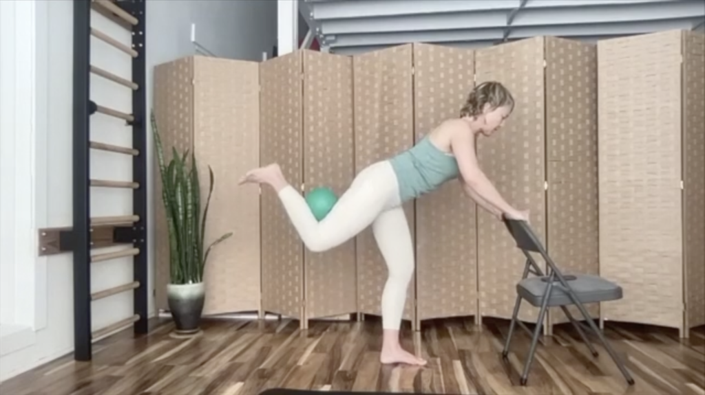 Woman doing Pilates exercises with a ball. She is holding on to a chair.