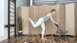 Woman doing Pilates exercises with a ball. She is holding on to a chair.