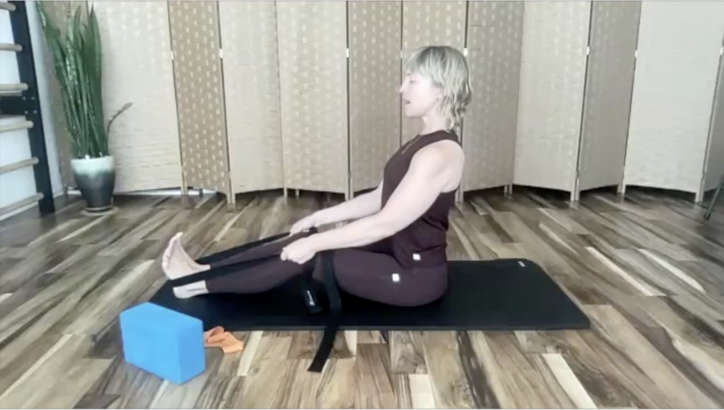 Woman doing Pilates exercises on a mat. She is using a yoga strap.