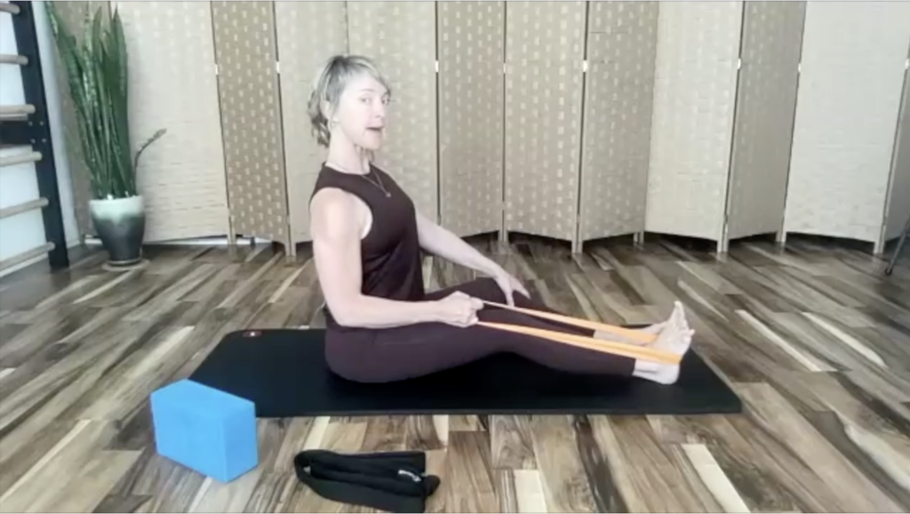 Woman doing Pilates exercises on a mat. She is using a loop band.