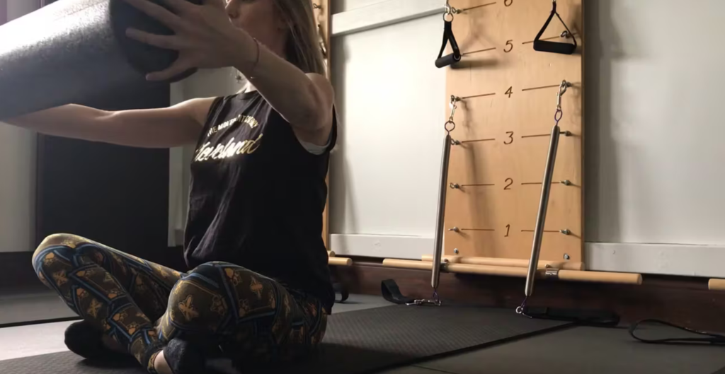 Woman doing Pilates exercises in a Pilates studio. She is holding a foam roller.