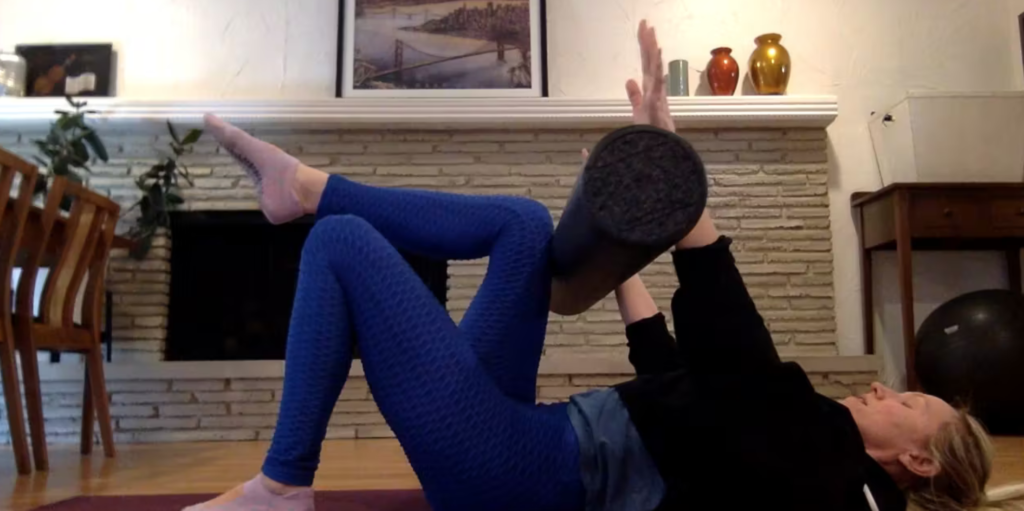 Woman doing Pilates abdominal exercises on the Pilates mat with a foam roller.