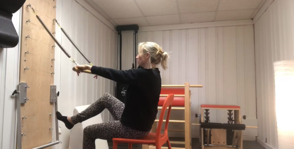 Woman doing Pilates with a springboard sitting on a chair.