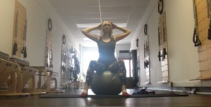 Woman doing Pilates exercises on a yoga mat with a Pilates ball in a Pilates studio.