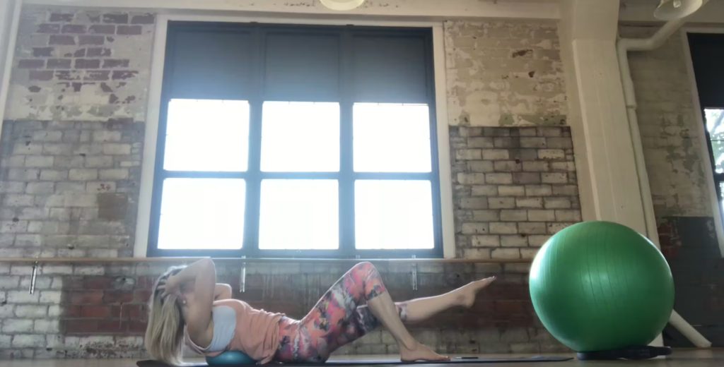 Woman doing Pilates exercises on a yoga mat with a Pilates ball in a Pilates studio.