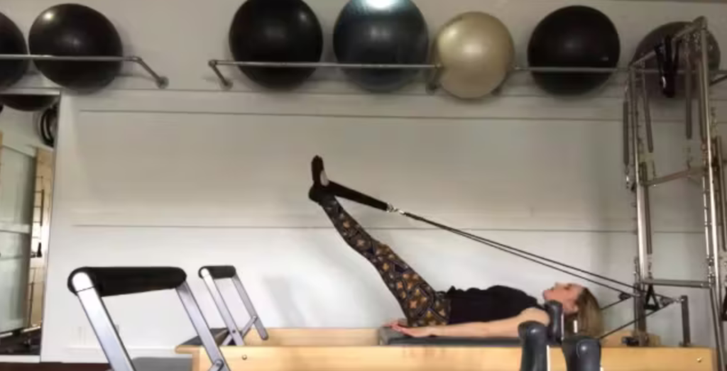 Woman doing Pilates reformer exercises with feet in straps in a Pilates studio.