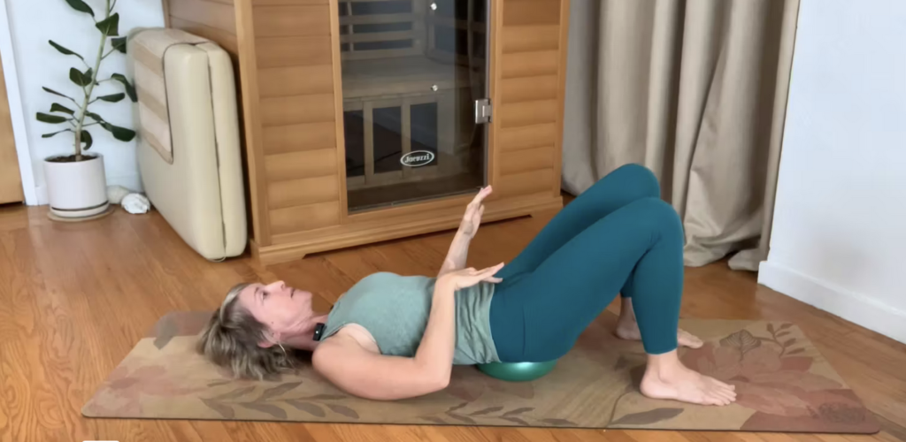 Woman doing Pilates mat exercises on the floor lying on her back with small squishy ball