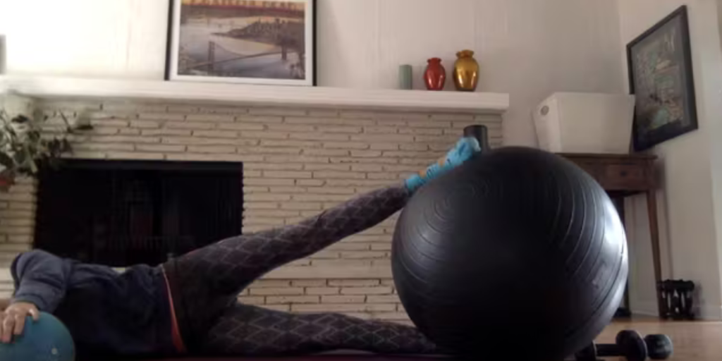 Woman lying on the floor doing Pilates exercises with a stability ball and small ball