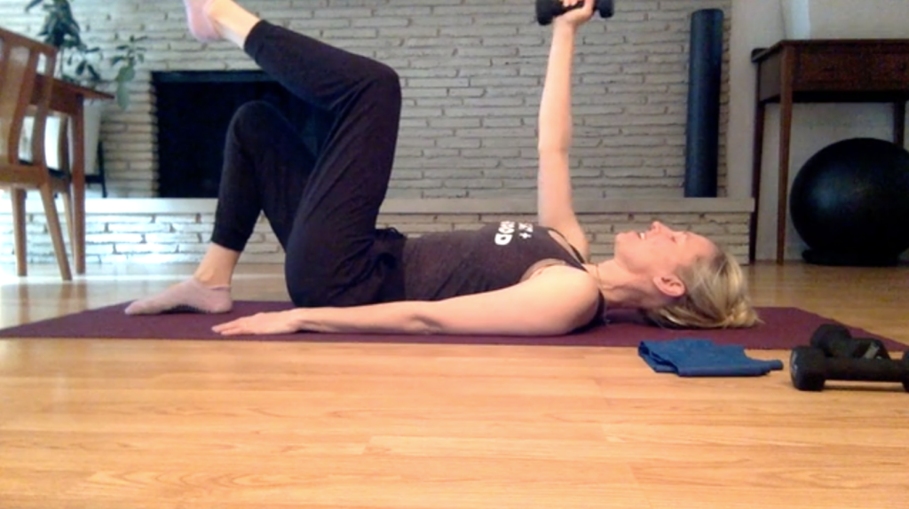 Woman doing Pilates exercises on the floor holding weight in hand for fitness and strength