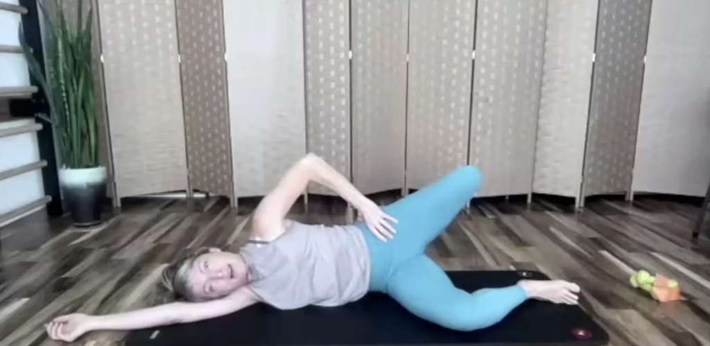 Woman doing Pilates exercises on the floor lying on her side reaching her leg back