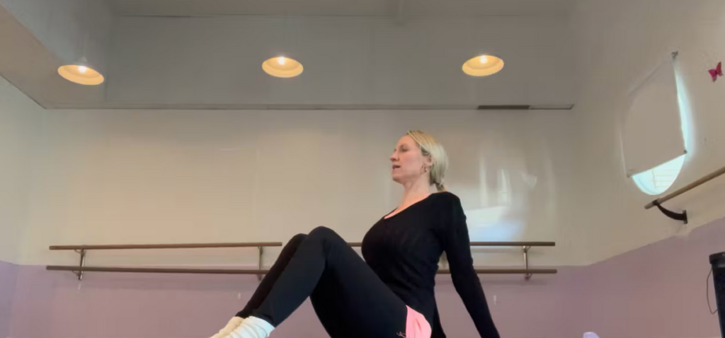 Woman doing Pilates seated on a mat. She is in a dance studio.