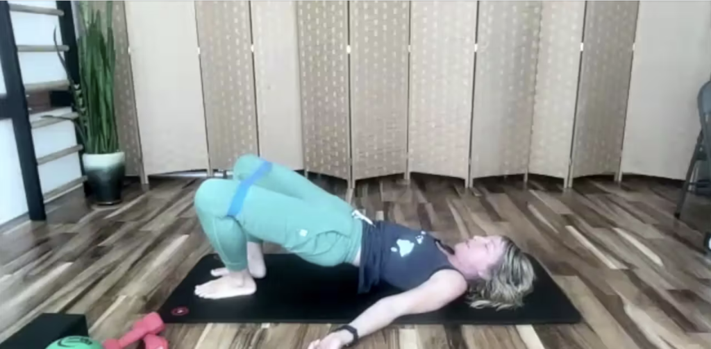 Woman doing Pilates exercises on a yoga mat. She has a loop band on her legs.