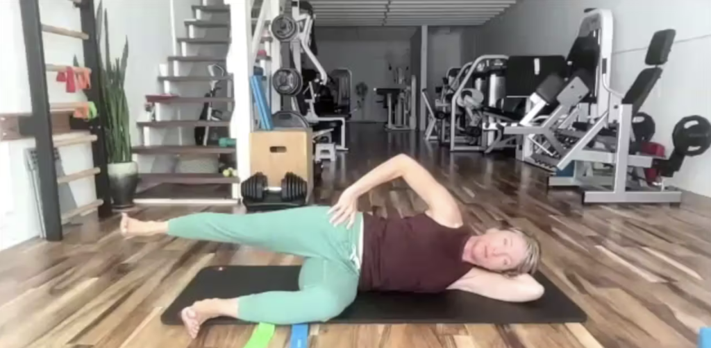 Woman doing Pilates leg lifts on her yoga mat. She is in a gym.