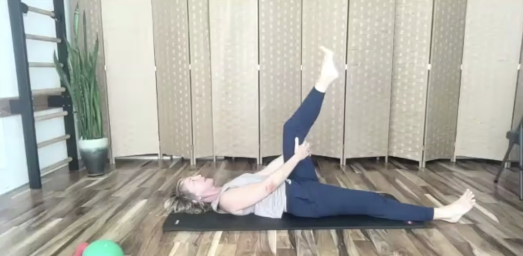 Woman doing Pilates exercises. She is holding her leg in the air.