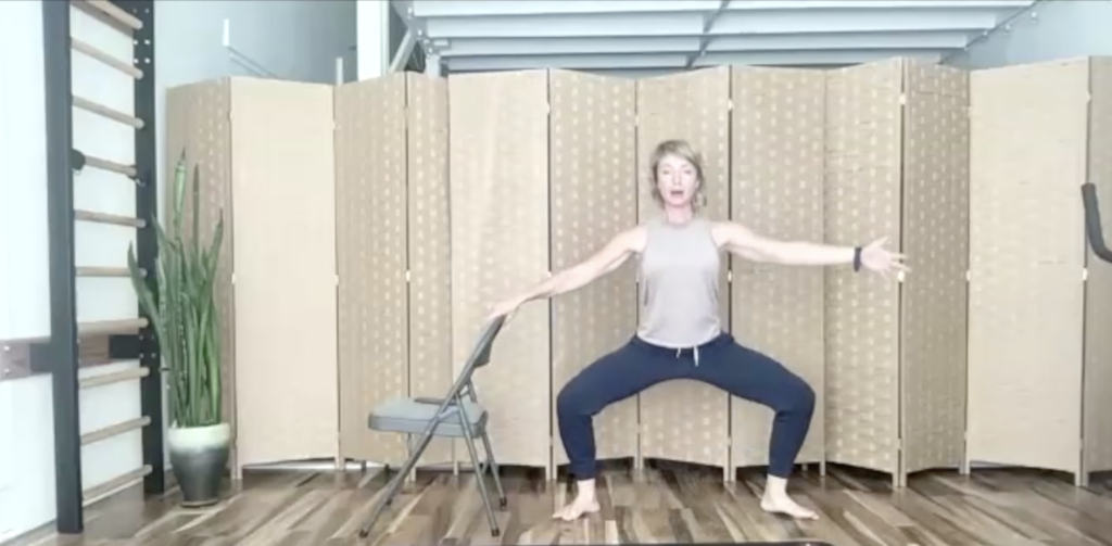 Woman doing standing Pilates and barre exercises with a chair.