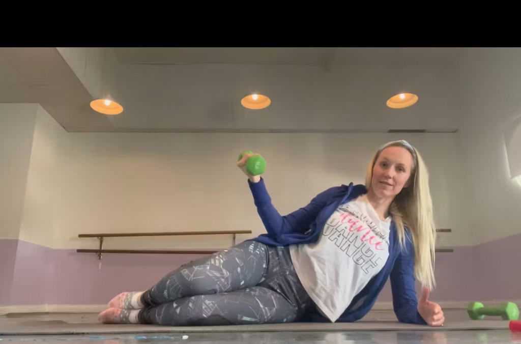 Woman doing Pilates exercises lying on her side on her Pilates mat. There is a weight in her hand.