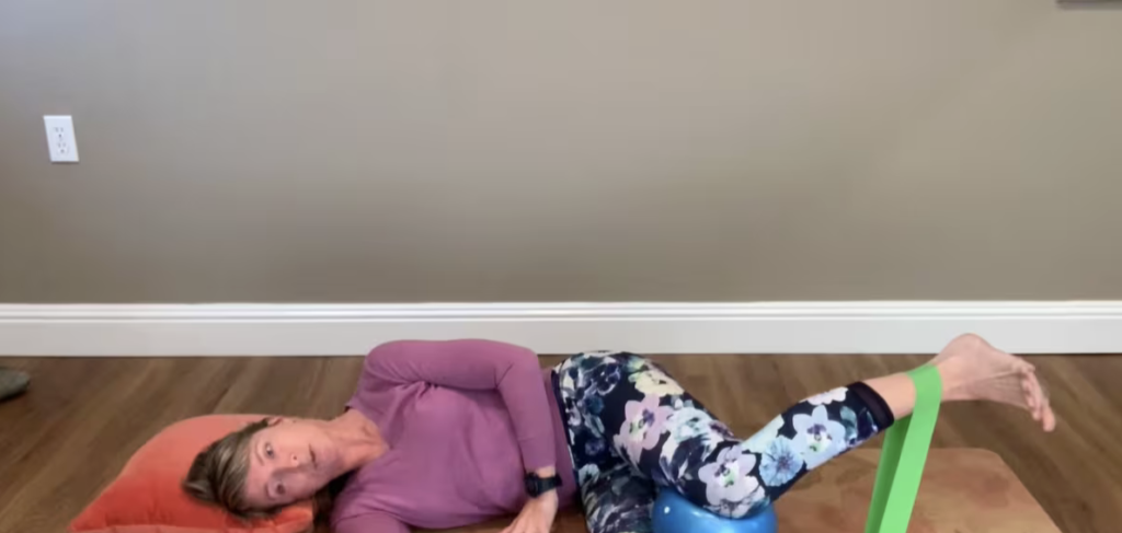 Woman doing Pilates mat exercises on the floor lying on her side with a ball and band