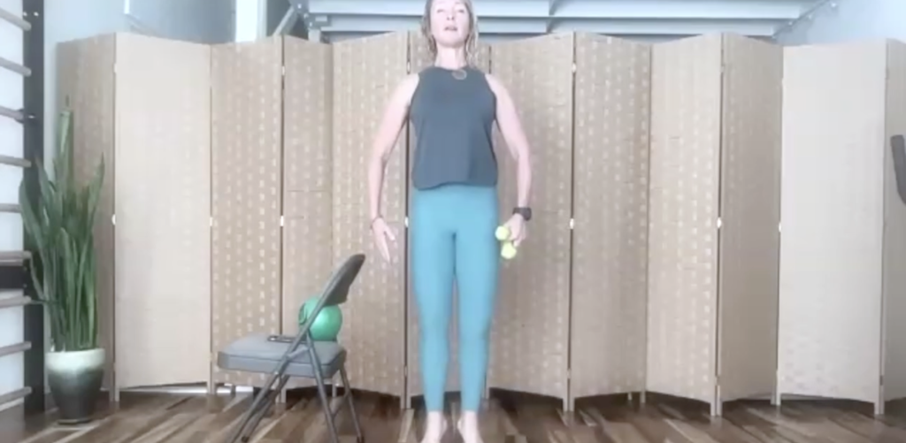 Woman standing doing Pilates and barre exercises. There are weights in her hand.