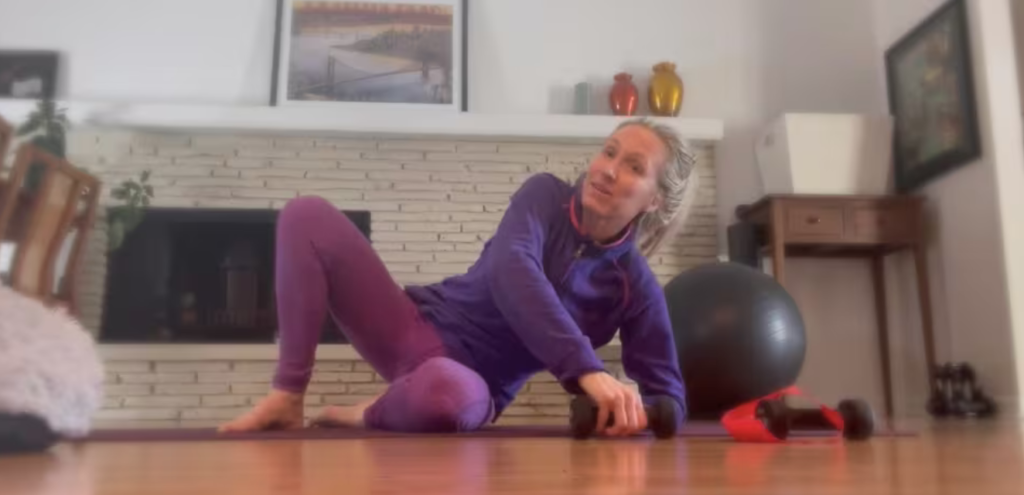 Woman doing Pilates exercises lying on her side on her Pilates mat. She is holding weights.