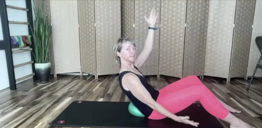 Woman doing Pilates exercises on the Pilates mat with a ball behind her back.