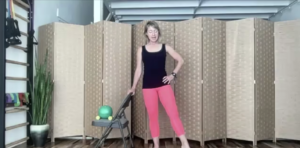 Woman doing barre exercises standing holding a chair. One leg is extended like ballet.