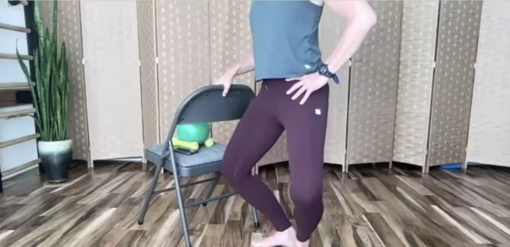 Woman standing holding on to a chair doing Pilates and barre exercises.