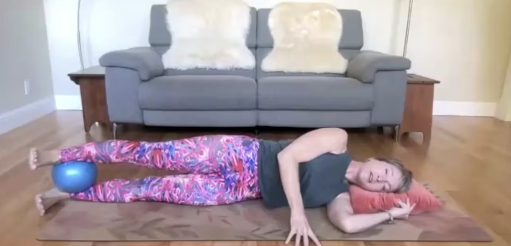 Woman doing Pilates exercises lying on her side on her Pilates mat. There is a ball between her ankles.