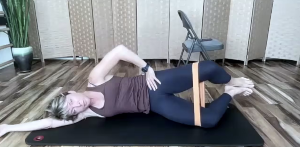 Woman lying on her side on a yoga mat doing PIlates clam exercises with loop band.