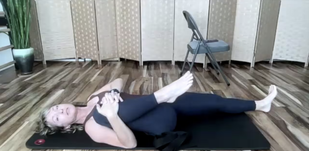 Woman doing Pilates exercises on a yoga mat hugging one knee.