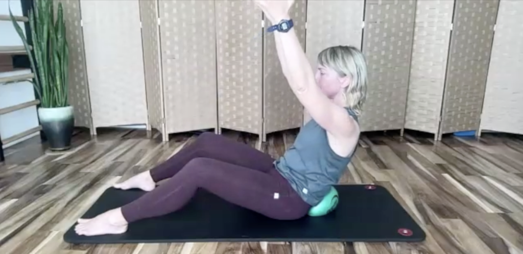 Woman doing Pilates exercises on the floor. There is a ball behind her back.