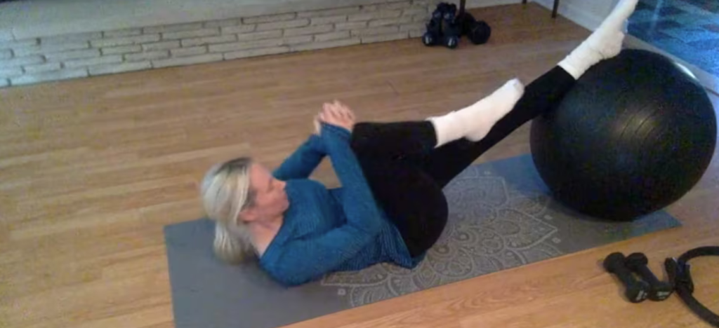 Woman doing Pilates abdominal exercises wtih feet on a big ball on a yoga mat.