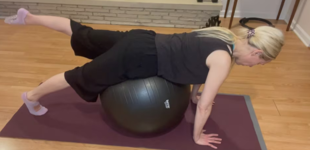 Woman doing Pilates exercises in a plank over a big ball with one leg lifted up.