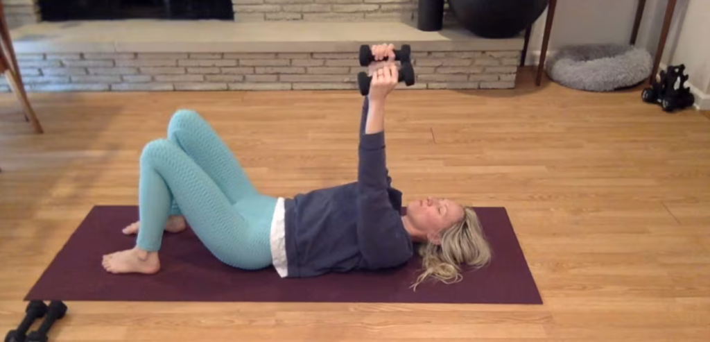 Woman doing Pilates exercises on the Pilates mat holding weights in her arms.