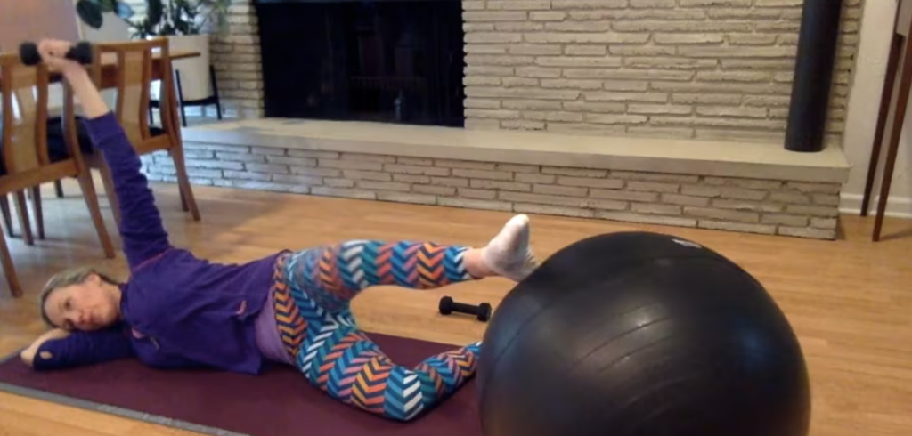 Woman doing Pilates exercises lying on her side with a weight and PIlates ball.