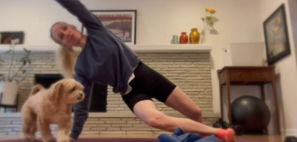 Woman doing Pilates exercises on a pilates mat. There is a small dog in the photo next to the woman.