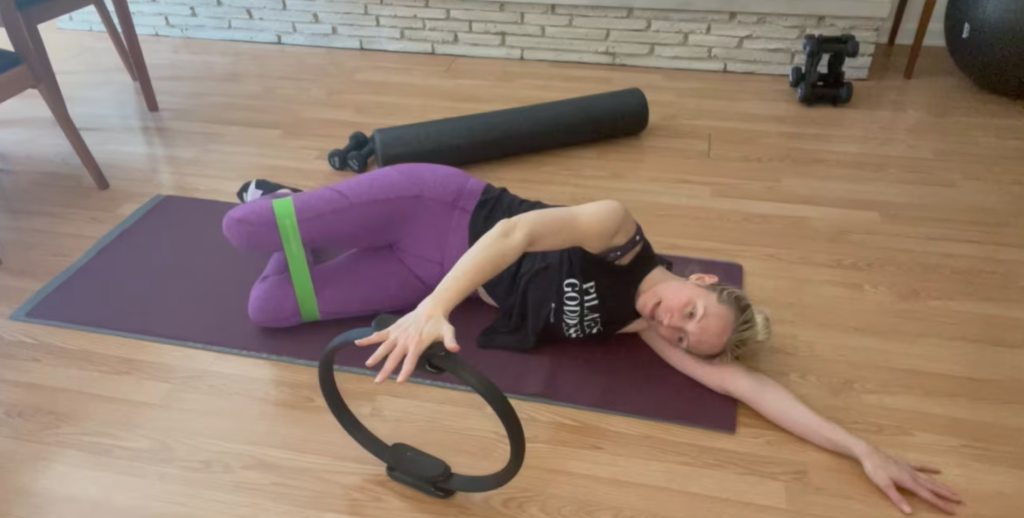 Woman lying on her side on the Pilates mat doing Pilates exercises with Pilates magic circle and Loop band.