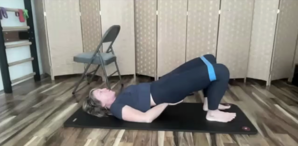 Woman doing Pilates bridging exercises on the floor with a loop band for fitness strength and balance