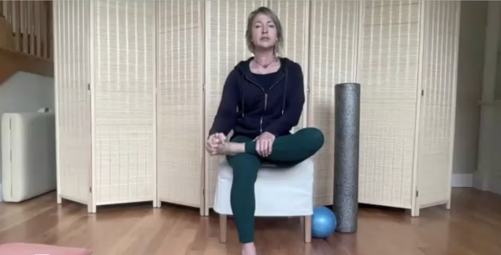 Woman doing Pilates sitting in a chair with one leg over stretching her foot.