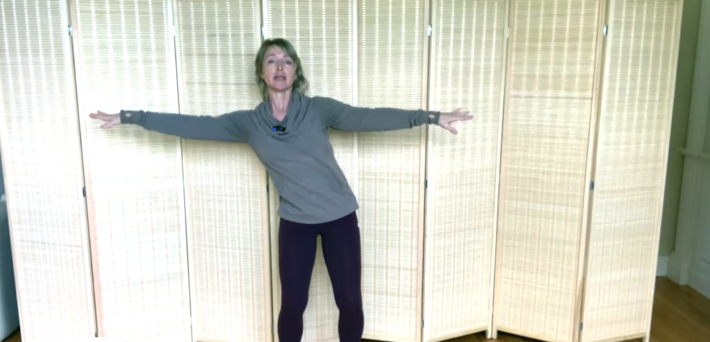 Woman standing doing Pilates exercises. She is reaching to one side.