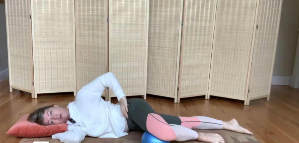 Woman lying on her side on her Pilates mat doing Pilates exercises with a ball under her front leg.