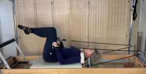 Woman on the Pilates reformer lying on the reformer doing tricep exercises.