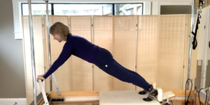 Woman doing Plank position on Pilates reformer. Her hands are on the foot bar and she is working her core muscles.