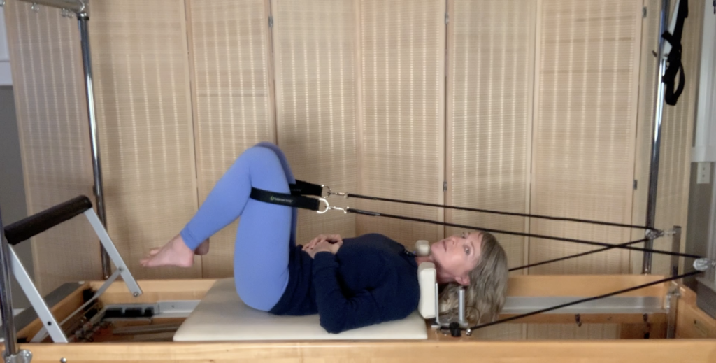 Woman doing Pilates exercises on the Pilates reformer. Her legs are in the Pilates loops and she is working her muscles with exercise.