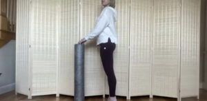 Woman standing with foam roller doing Pilates exercises.